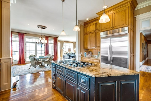 kitchen with pendant lighting, crown molding, stainless steel appliances, light stone counters, and a kitchen island