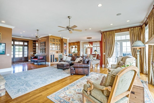 living room featuring ornamental molding, ceiling fan with notable chandelier, and light hardwood / wood-style flooring