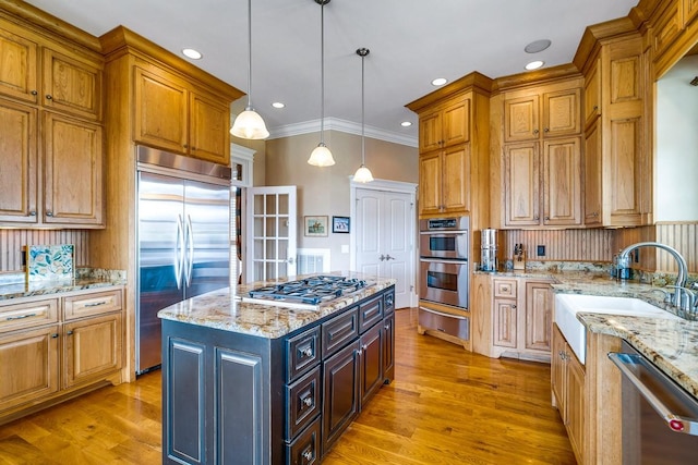 kitchen featuring sink, light stone counters, appliances with stainless steel finishes, a kitchen island, and pendant lighting