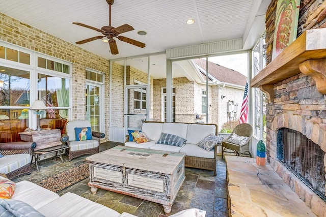 sunroom with ceiling fan and an outdoor stone fireplace