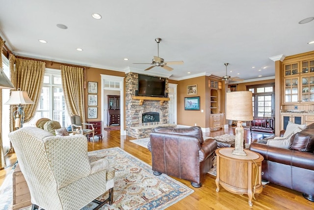 living room with ornamental molding, ceiling fan, a fireplace, and light hardwood / wood-style floors