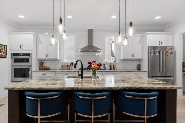 kitchen featuring white cabinetry, a center island with sink, wall chimney exhaust hood, and appliances with stainless steel finishes