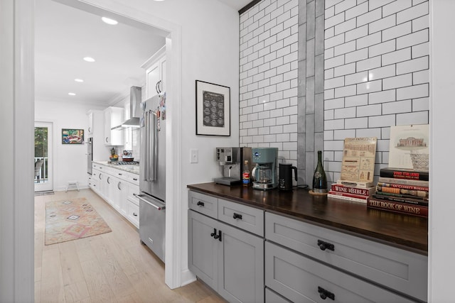 kitchen featuring stainless steel appliances, white cabinetry, wall chimney range hood, and light hardwood / wood-style floors