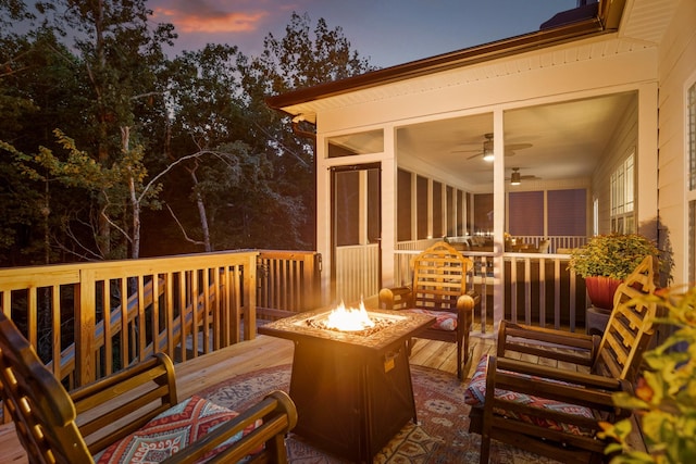 deck at dusk featuring a sunroom, ceiling fan, and an outdoor fire pit