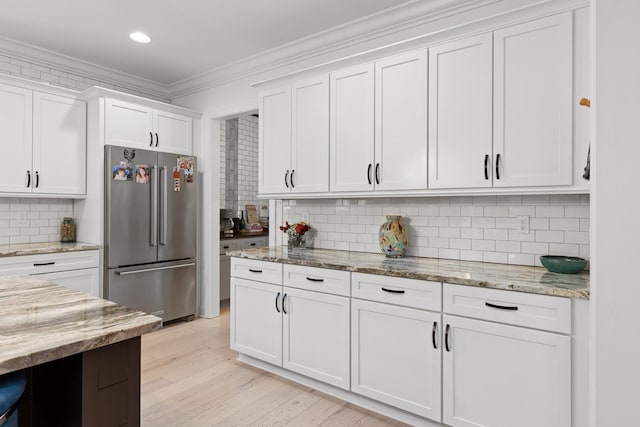 kitchen featuring white cabinetry, light stone counters, crown molding, and stainless steel refrigerator