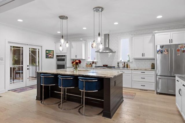 kitchen with wall chimney range hood, a center island, white cabinets, and appliances with stainless steel finishes