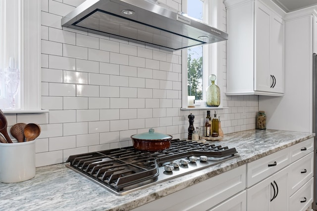 kitchen featuring wall chimney range hood, white cabinetry, backsplash, light stone countertops, and stainless steel gas cooktop