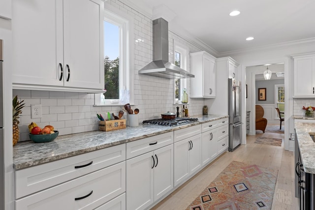 kitchen with wall chimney range hood, crown molding, white cabinetry, stainless steel appliances, and light stone counters