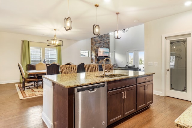 kitchen with an island with sink, sink, hanging light fixtures, stainless steel dishwasher, and light stone countertops