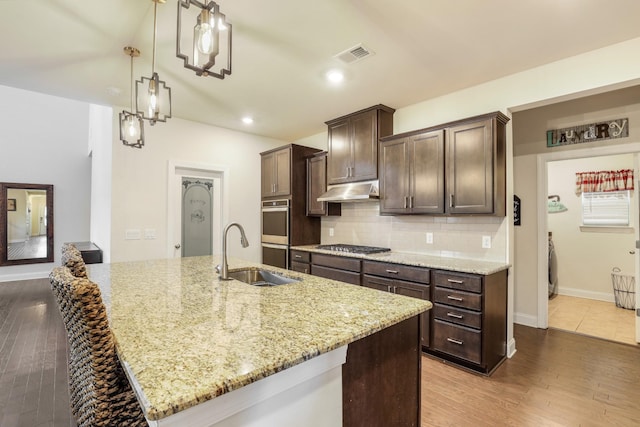 kitchen featuring a kitchen island with sink, sink, and light stone countertops