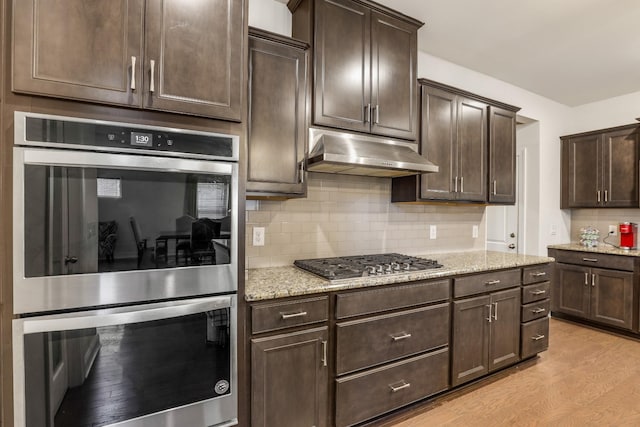 kitchen featuring appliances with stainless steel finishes, light stone counters, and dark brown cabinetry