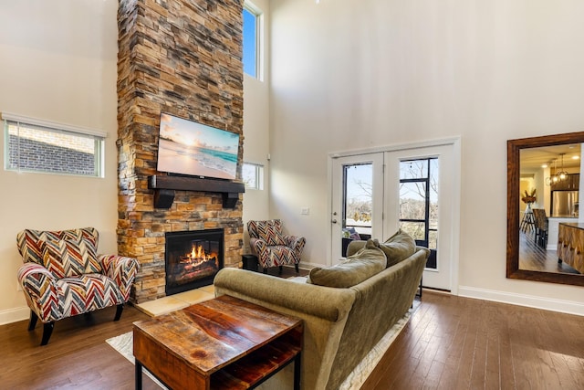 living room with a stone fireplace, a towering ceiling, hardwood / wood-style floors, and french doors