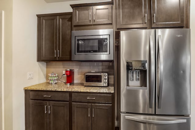 kitchen with appliances with stainless steel finishes, light stone countertops, dark brown cabinets, and backsplash