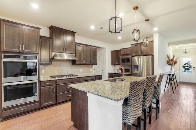 kitchen featuring pendant lighting, sink, decorative backsplash, stainless steel appliances, and light stone countertops