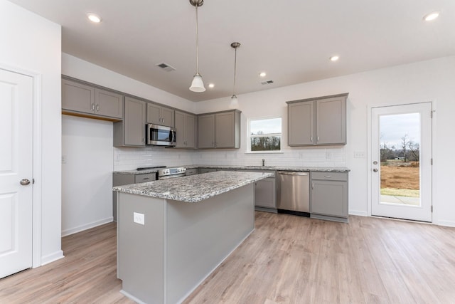 kitchen with a center island, appliances with stainless steel finishes, gray cabinets, pendant lighting, and light stone countertops