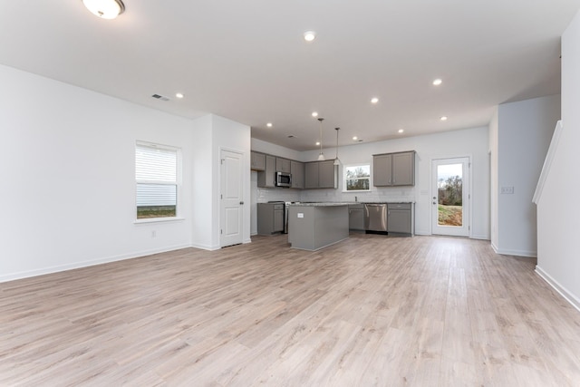 kitchen with gray cabinetry, hanging light fixtures, a kitchen island, stainless steel appliances, and light hardwood / wood-style floors