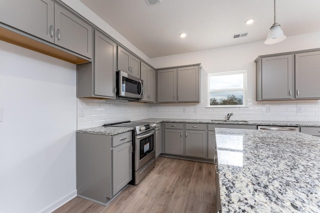 kitchen with gray cabinets, hanging light fixtures, stainless steel appliances, light stone counters, and decorative backsplash