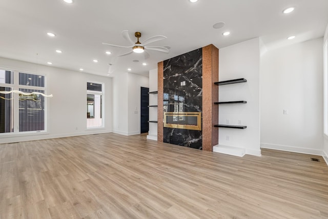 unfurnished living room with a premium fireplace, ceiling fan, and light wood-type flooring