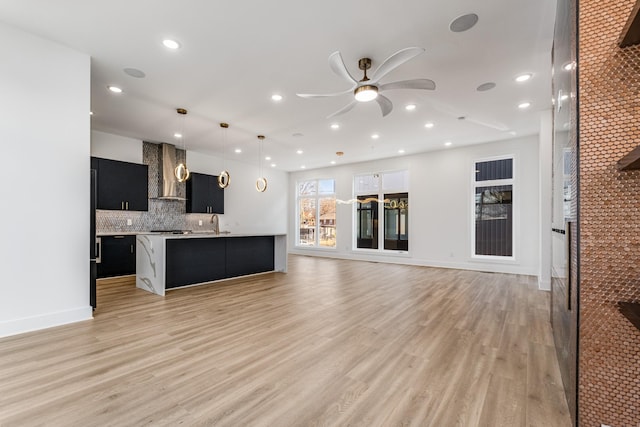 kitchen featuring pendant lighting, an island with sink, decorative backsplash, wall chimney exhaust hood, and light hardwood / wood-style flooring