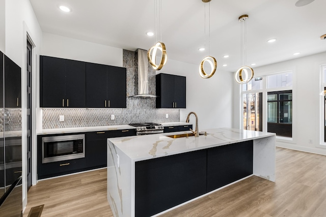 kitchen featuring hanging light fixtures, a kitchen island with sink, wall chimney range hood, and stainless steel appliances