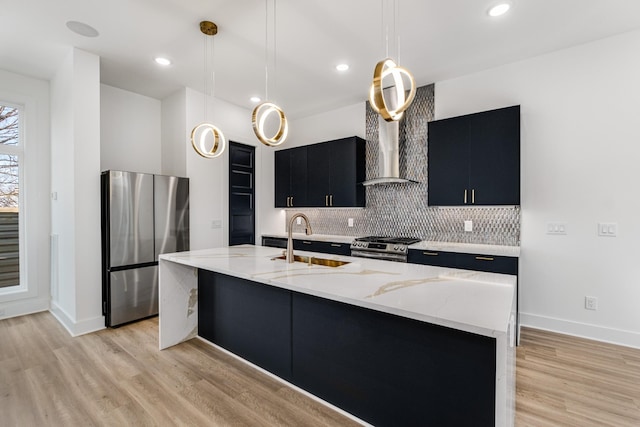 kitchen featuring pendant lighting, stainless steel appliances, an island with sink, and wall chimney range hood