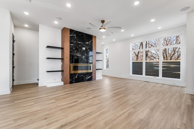 unfurnished living room featuring ceiling fan, a premium fireplace, and light hardwood / wood-style floors