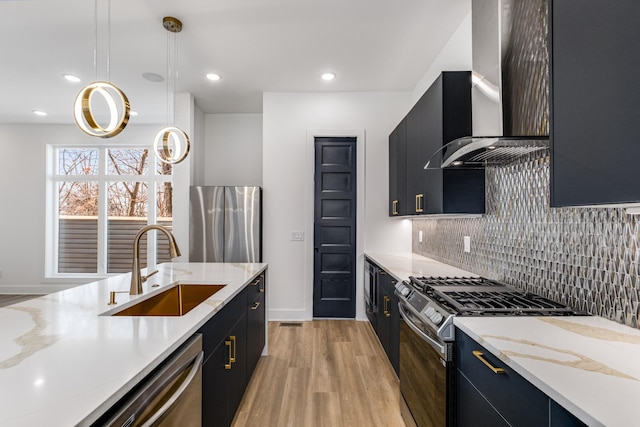 kitchen featuring sink, light hardwood / wood-style flooring, appliances with stainless steel finishes, hanging light fixtures, and wall chimney exhaust hood