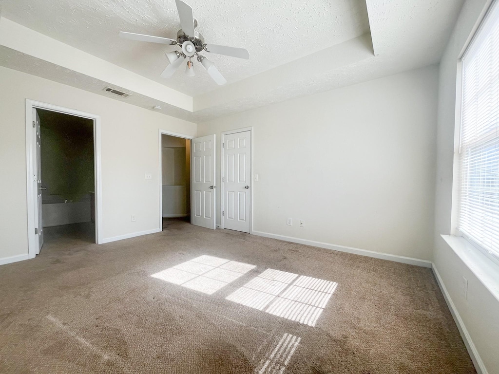 unfurnished bedroom with ensuite bathroom, a tray ceiling, light carpet, and a textured ceiling