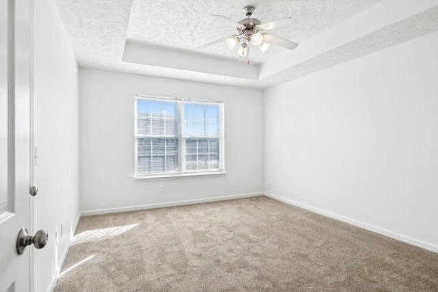 spare room with carpet, a raised ceiling, a textured ceiling, and baseboards