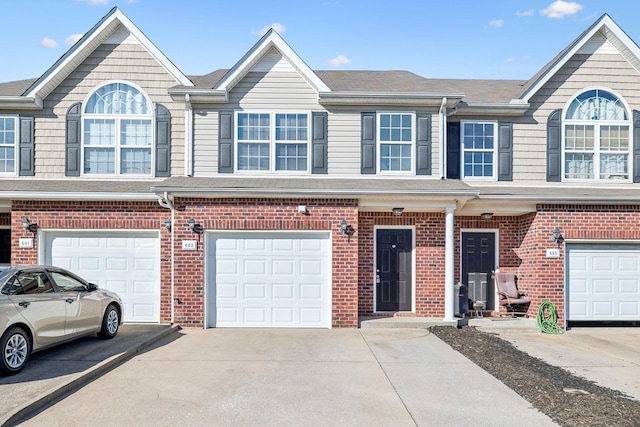 view of property with a garage, driveway, brick siding, and roof with shingles