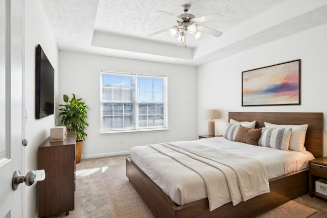 bedroom featuring a raised ceiling, light carpet, a textured ceiling, and baseboards