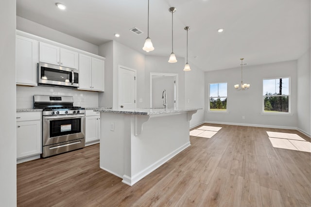 kitchen featuring pendant lighting, stainless steel appliances, light stone countertops, white cabinets, and a center island with sink