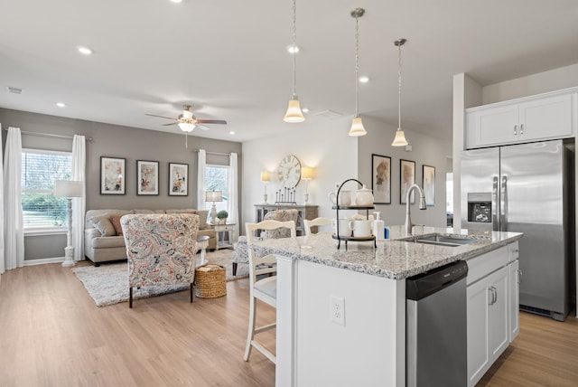 kitchen featuring sink, white cabinetry, appliances with stainless steel finishes, light stone countertops, and a kitchen island with sink