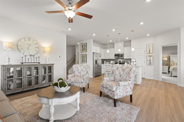 living room featuring sink, ceiling fan, and light wood-type flooring