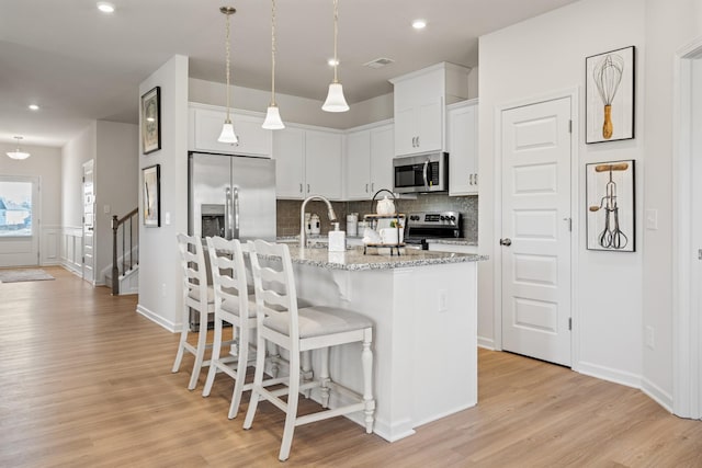 kitchen featuring white cabinetry, appliances with stainless steel finishes, a kitchen island with sink, and pendant lighting