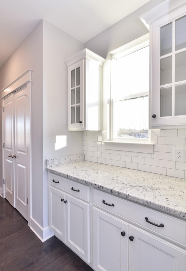 kitchen with tasteful backsplash, light stone countertops, white cabinets, and dark hardwood / wood-style flooring