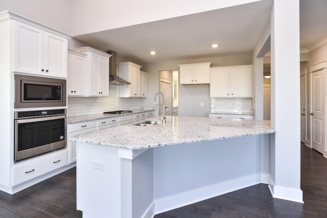 kitchen with sink, wall chimney range hood, appliances with stainless steel finishes, white cabinetry, and light stone counters