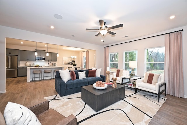 living room featuring ceiling fan with notable chandelier and light wood-type flooring