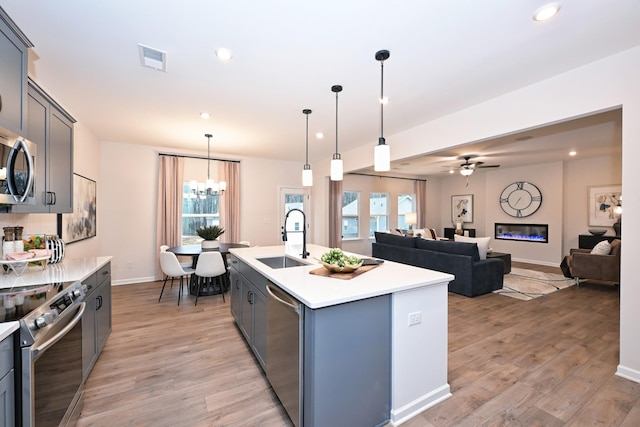 kitchen featuring sink, decorative light fixtures, a center island with sink, stainless steel appliances, and light hardwood / wood-style floors