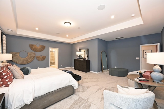 bedroom featuring light carpet, a tray ceiling, and ensuite bathroom