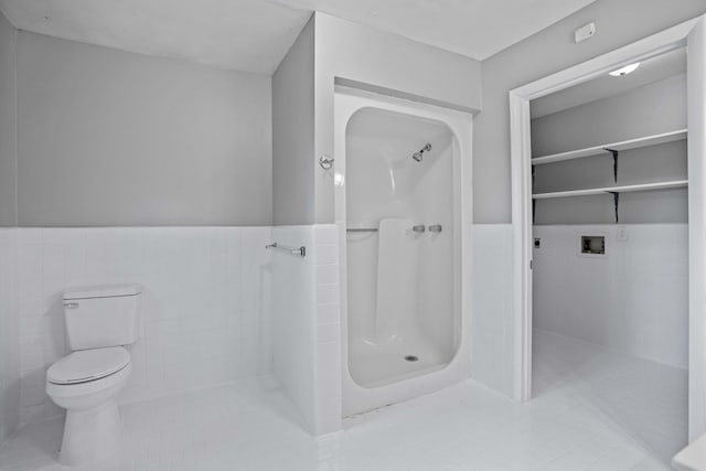 bathroom featuring tile patterned flooring, tiled shower, tile walls, and toilet