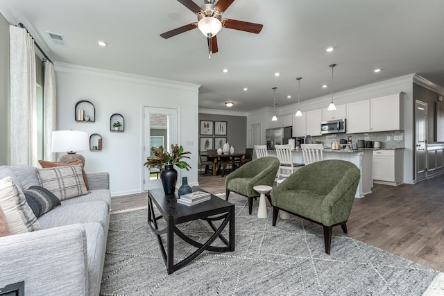 living room with wood-type flooring, ornamental molding, and ceiling fan