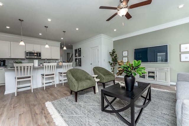 living room with crown molding, ceiling fan, and light wood-type flooring