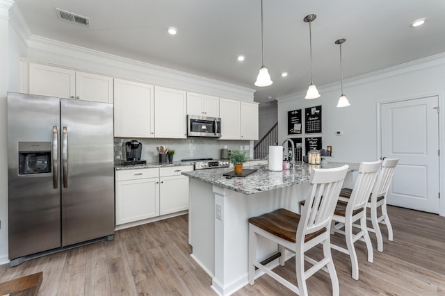 kitchen with stainless steel appliances, pendant lighting, a center island with sink, and white cabinets