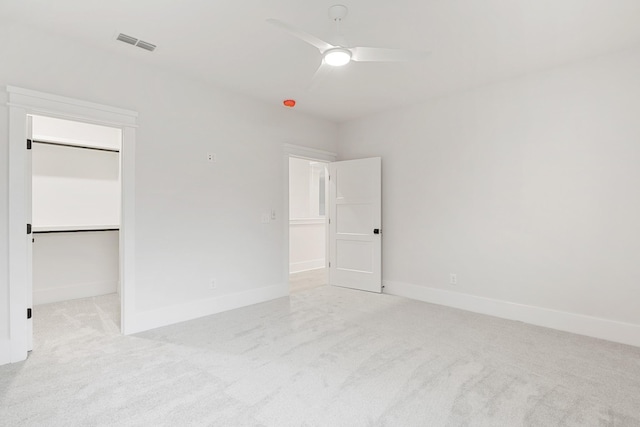 unfurnished bedroom featuring ceiling fan, a spacious closet, a closet, and light carpet