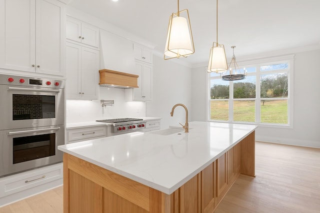 kitchen with an island with sink, sink, white cabinets, hanging light fixtures, and stainless steel appliances