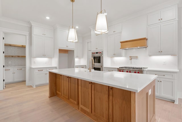 kitchen featuring white cabinetry, hanging light fixtures, stainless steel appliances, and a center island with sink