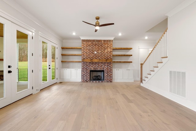 unfurnished living room featuring a brick fireplace, crown molding, french doors, and light wood-type flooring