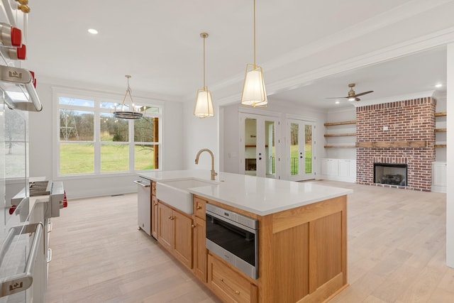 kitchen featuring decorative light fixtures, sink, a center island with sink, and light wood-type flooring