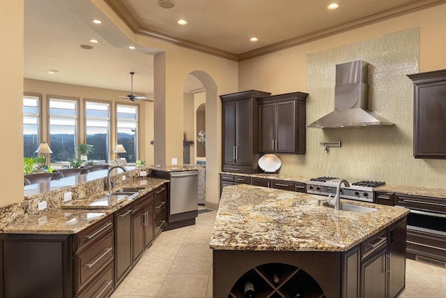 kitchen with a kitchen island with sink, wall chimney range hood, light stone counters, and stainless steel appliances